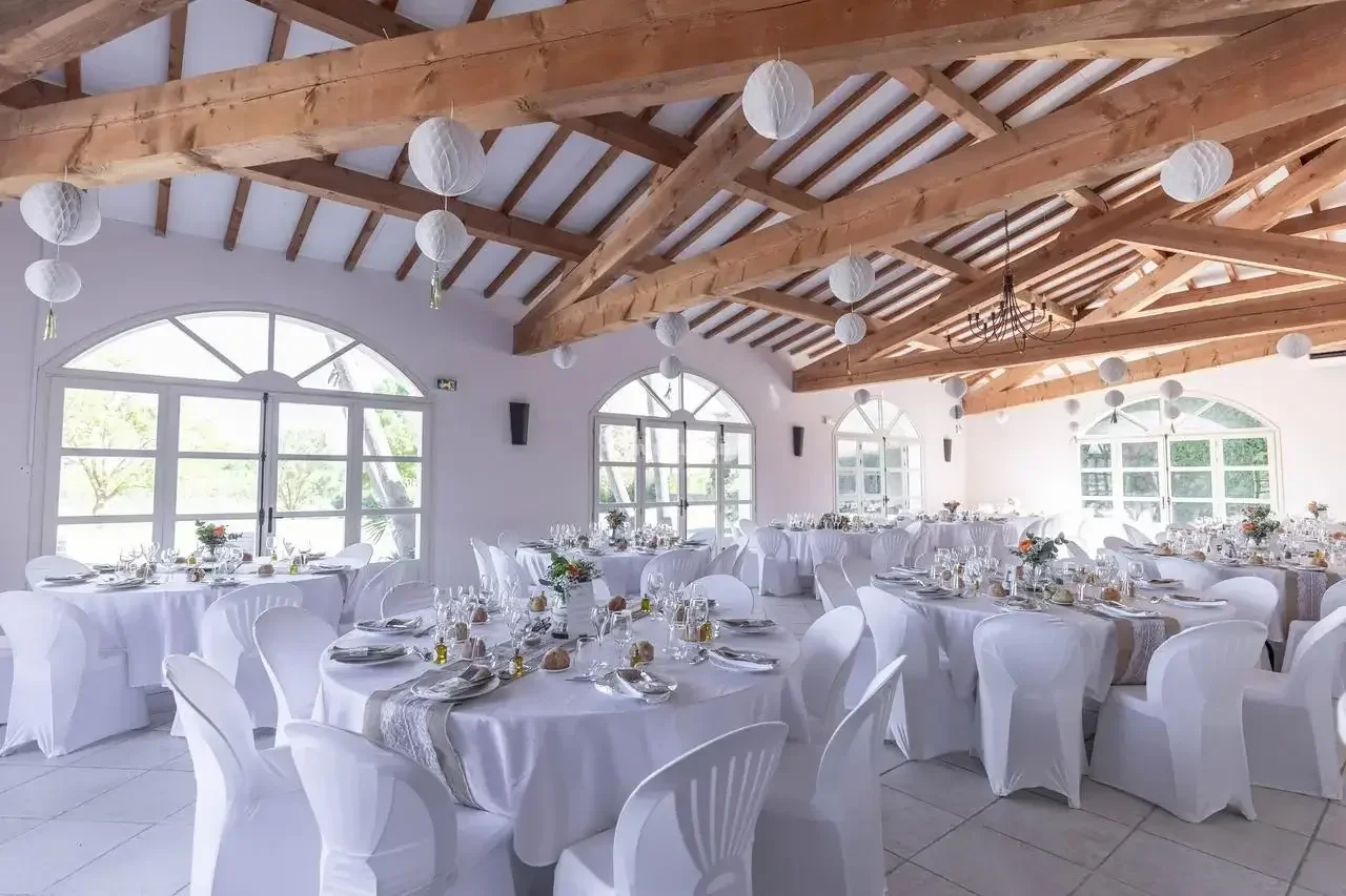 Grande salle réception poutres apparentes tables rondes dressées ambiance festive Bergerie de la Vernède Nissan-lez-Enserune mariage Hérault Occitanie