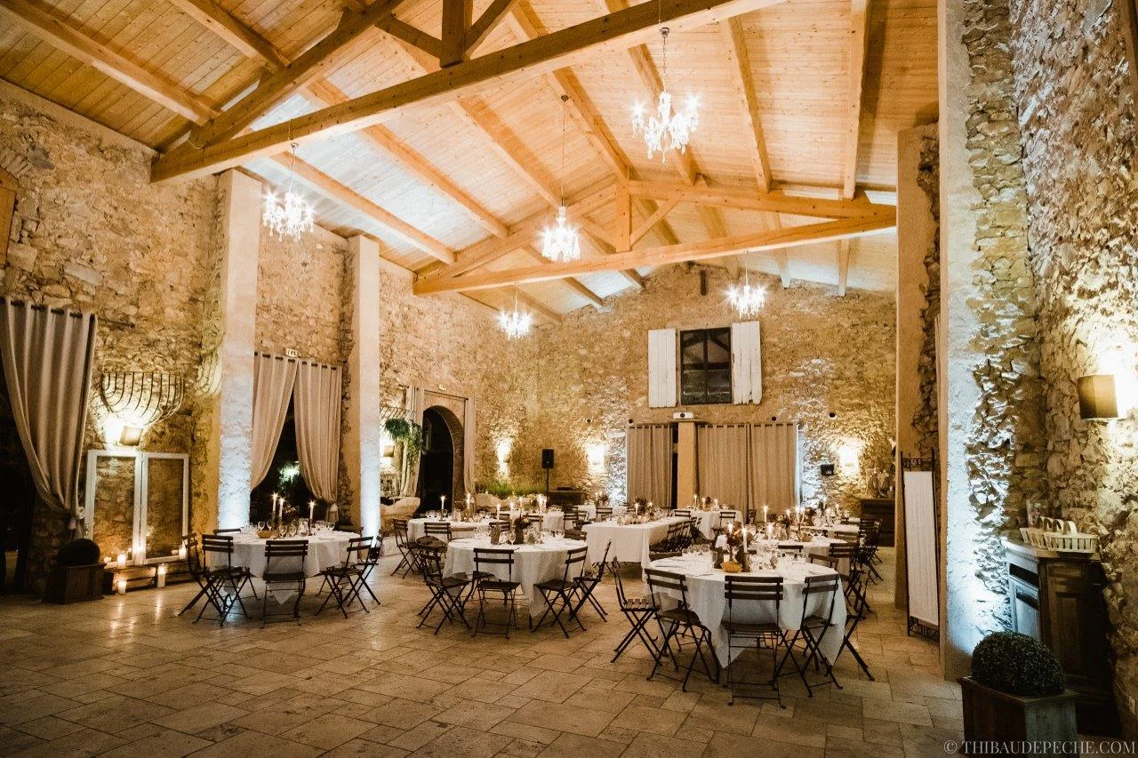 Salle de réception du Château Bas d'Aumelas en pierre avec lustres en cristal et tables dressées pour un mariage Hérault