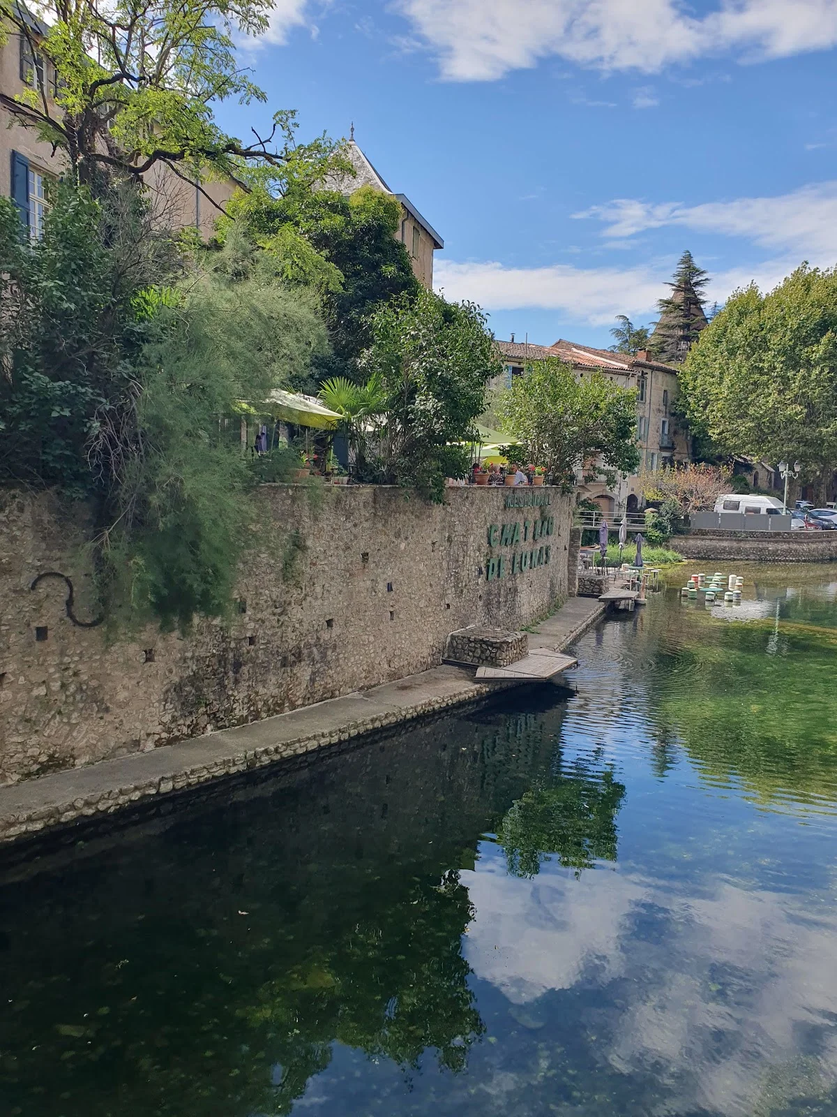 Façade du Château de Lunas le long de la rivière avec enseigne en pierre et reflets dans l'eau, Hérault