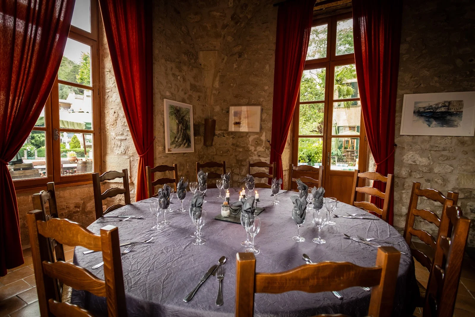 Salle de réception intérieure du Château de Lunas avec table ronde dressée, murs en pierre et rideaux rouges, Hérault