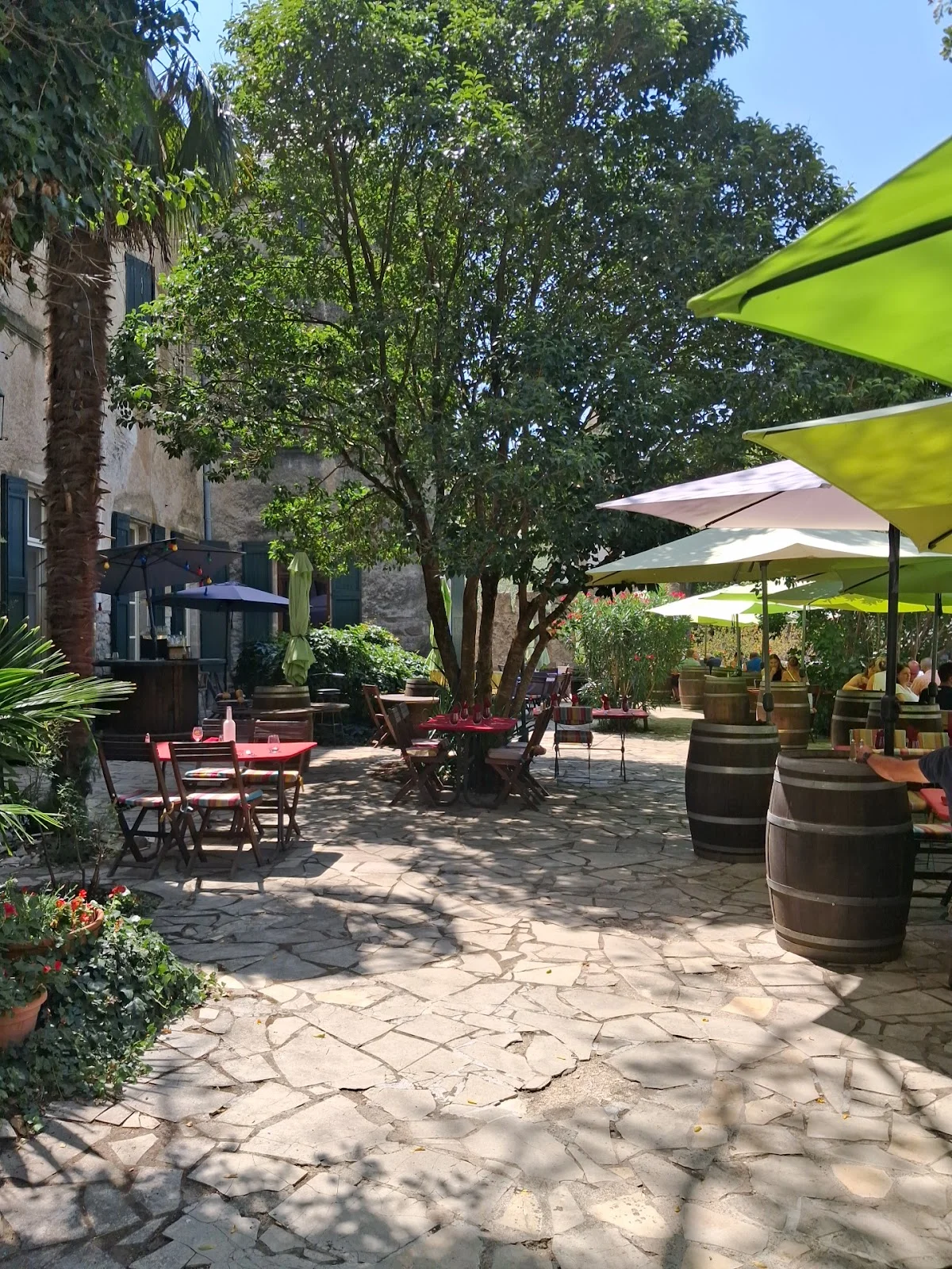 Terrasse jardin du Château de Lunas avec parasols, tonneaux et végétation méditerranéenne, restaurant Hérault