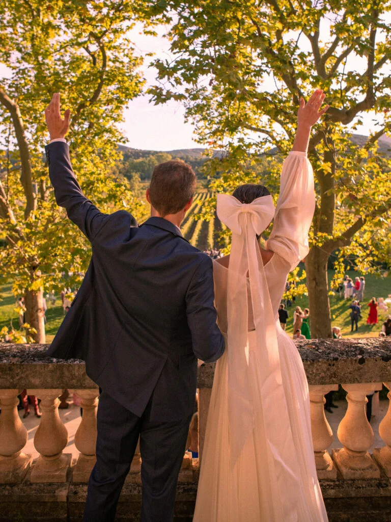 Mariés de dos levant les bras au coucher du soleil sur la terrasse du Château de Malmont, vignes Hérault