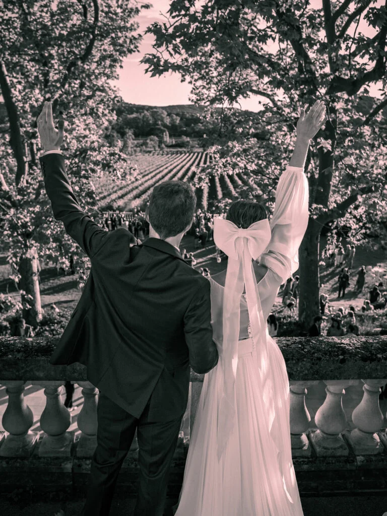 Mariés de dos levant les bras sur la terrasse du Château de Malmont avec vue sur les vignes, Hérault