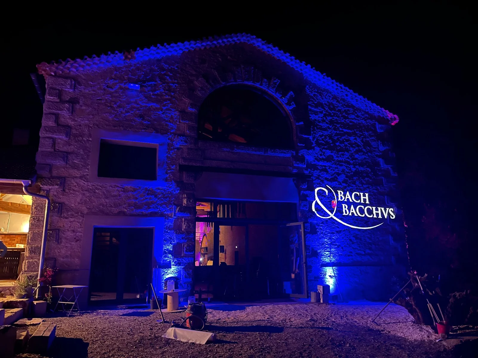 Façade du Château Domaine du Bosc illuminée en bleu la nuit avec enseigne Bach et Bacchus en Hérault