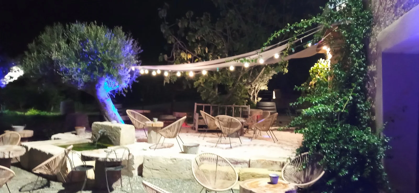 Terrasse lounge nocturne avec guirlandes lumineuses et fauteuils en rotin au Château Domaine du Bosc Hérault