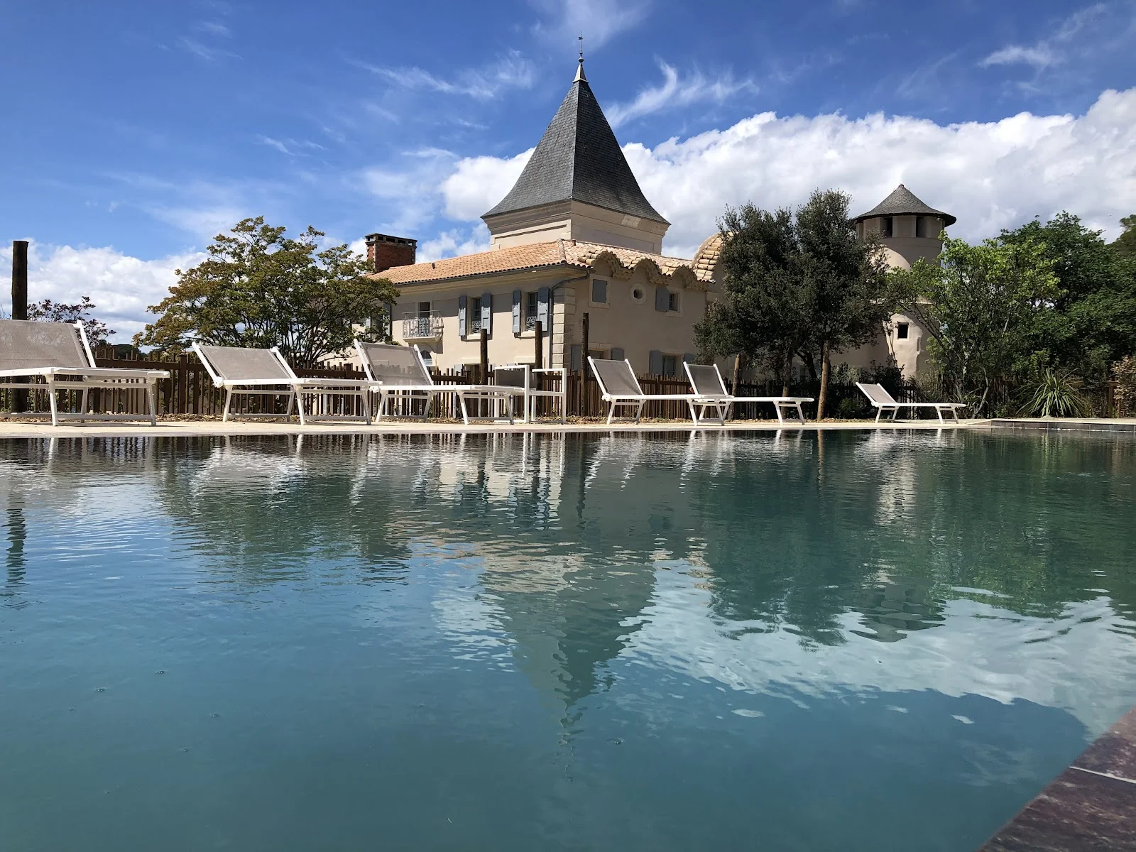 Piscine du Château du Parc avec reflet du château et transats blancs pour mariage dans l'Hérault