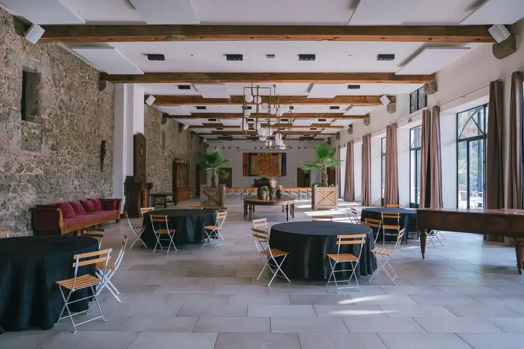 Grande salle réception Château Hermitage Combas Hérault vue frontale tables rondes mur pierre lustre design