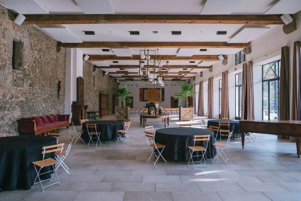 Grande salle de réception Château Hermitage de Combas Hérault mur pierre tables rondes et palmiers décoratifs