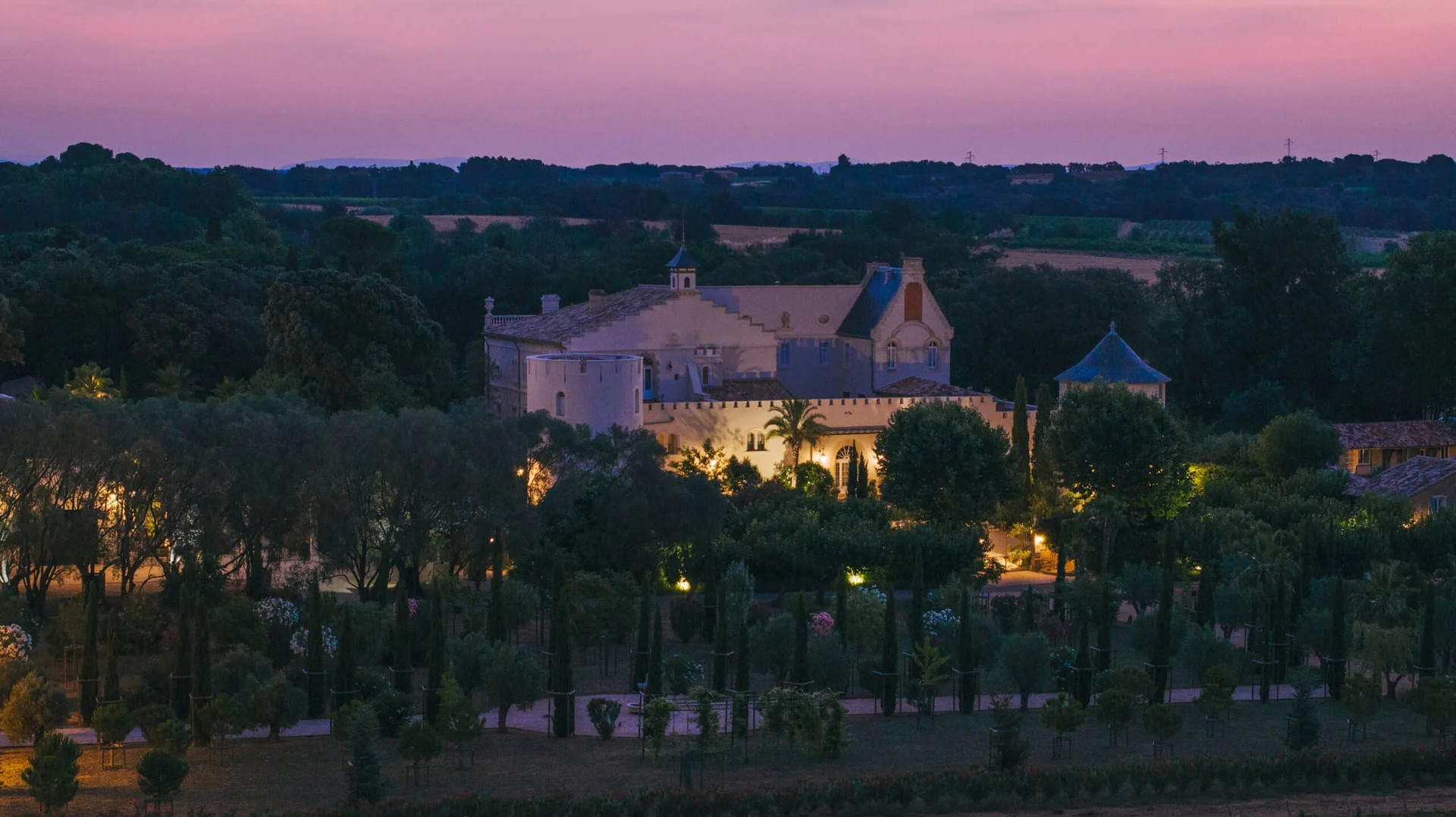 Vue aérienne nocturne Château Hermitage de Combas Hérault illuminé au coucher du soleil ciel rose
