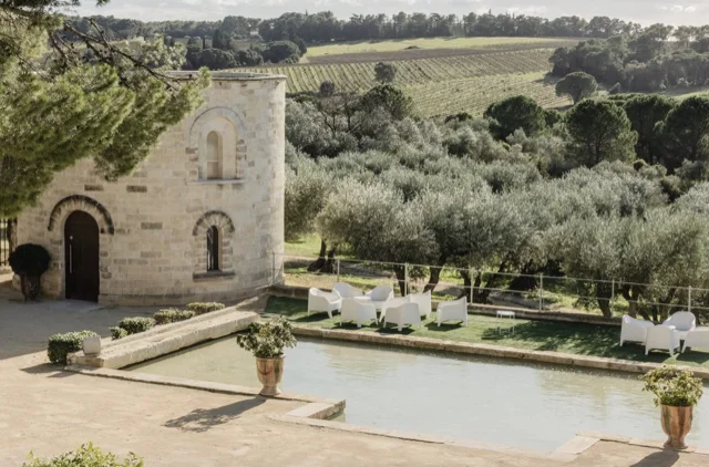 Bassin miroir et chapelle romane du Château Puech-Haut avec fauteuils blancs et oliviers, jardin idéal pour mariage en Hérault