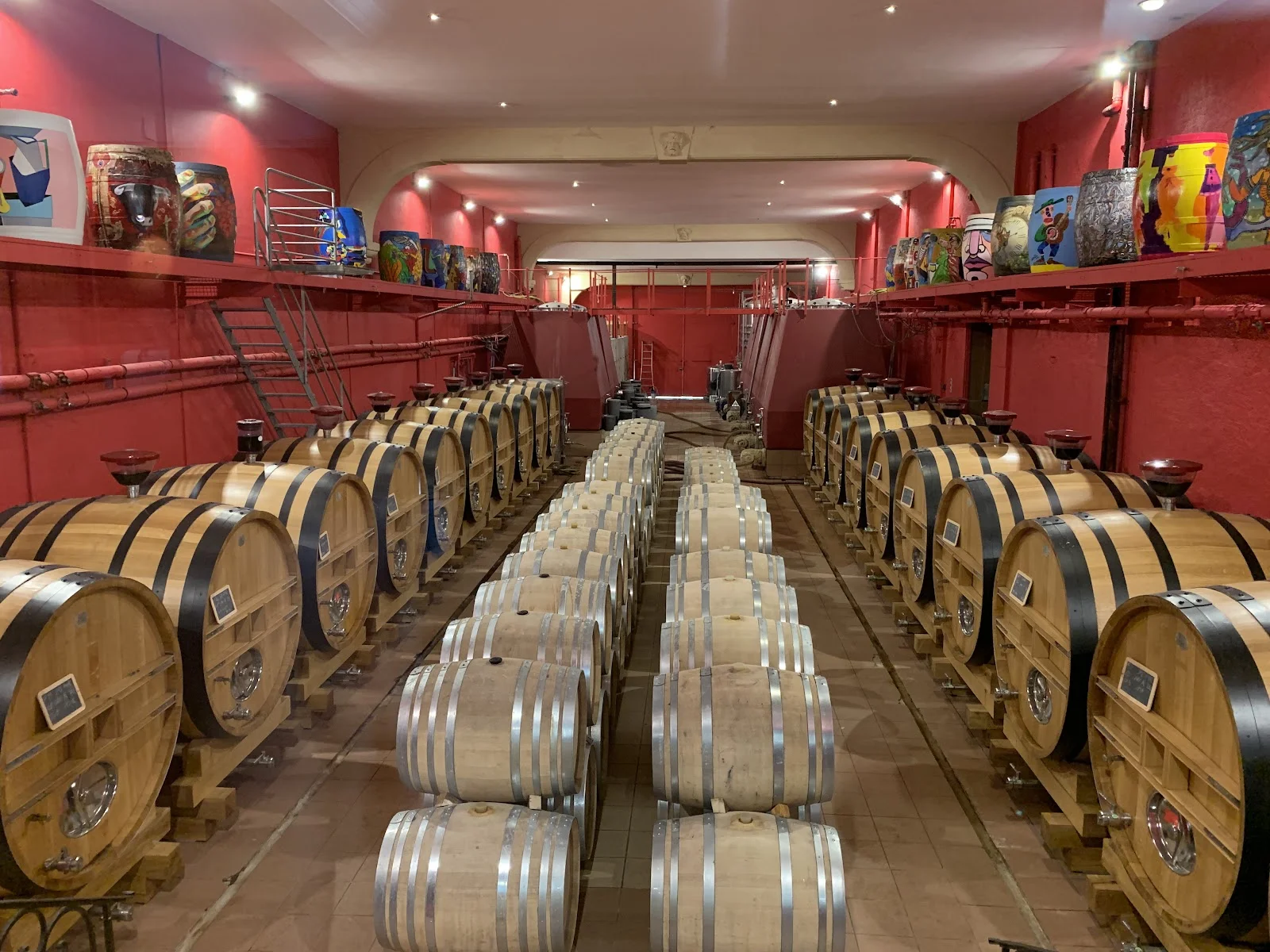 Cave à barriques rouge du Château Puech-Haut en Hérault avec fûts de chêne et art sur tonneaux, lieu de réception mariage