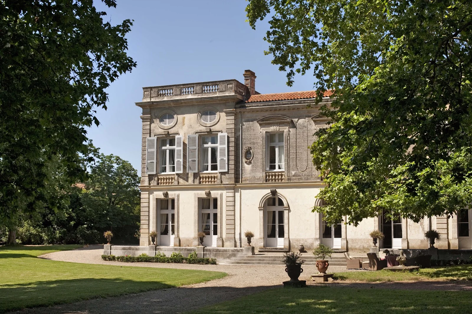 Façade principale néoclassique du Château Raissac dans l'Hérault en plein jour, parc arboré et allée gravillonnée