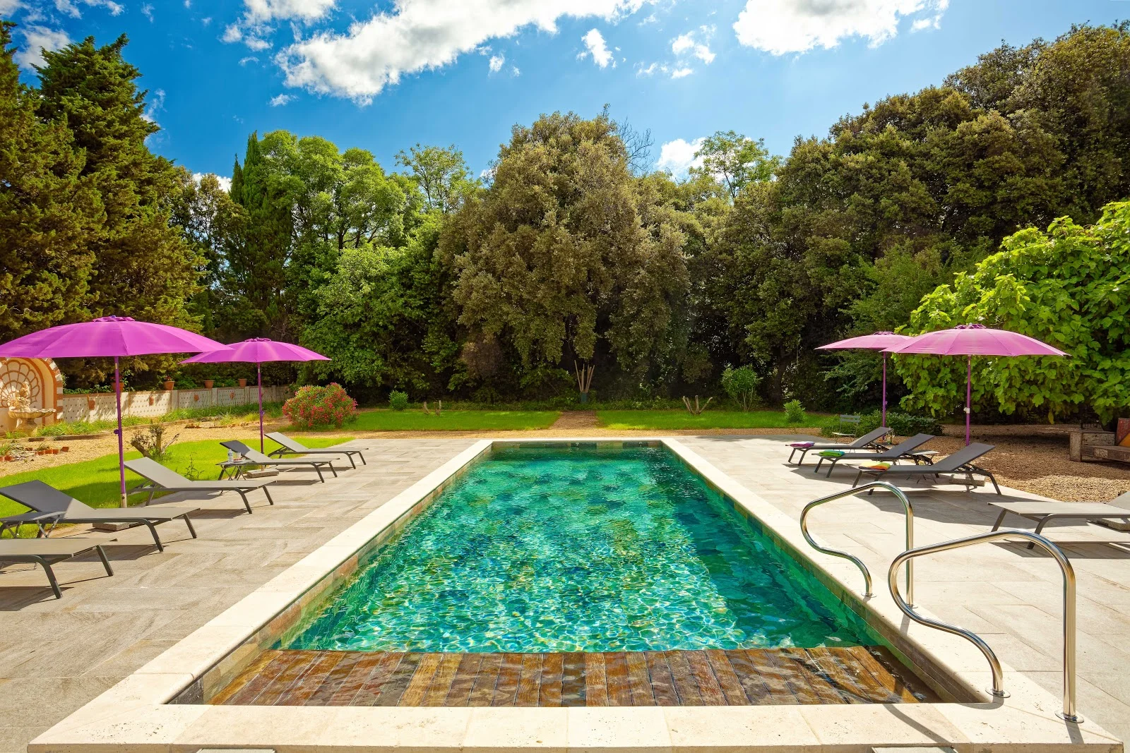Piscine turquoise du Château Raissac Hérault avec parasols fuchsia et jardin arboré pour mariage en plein air