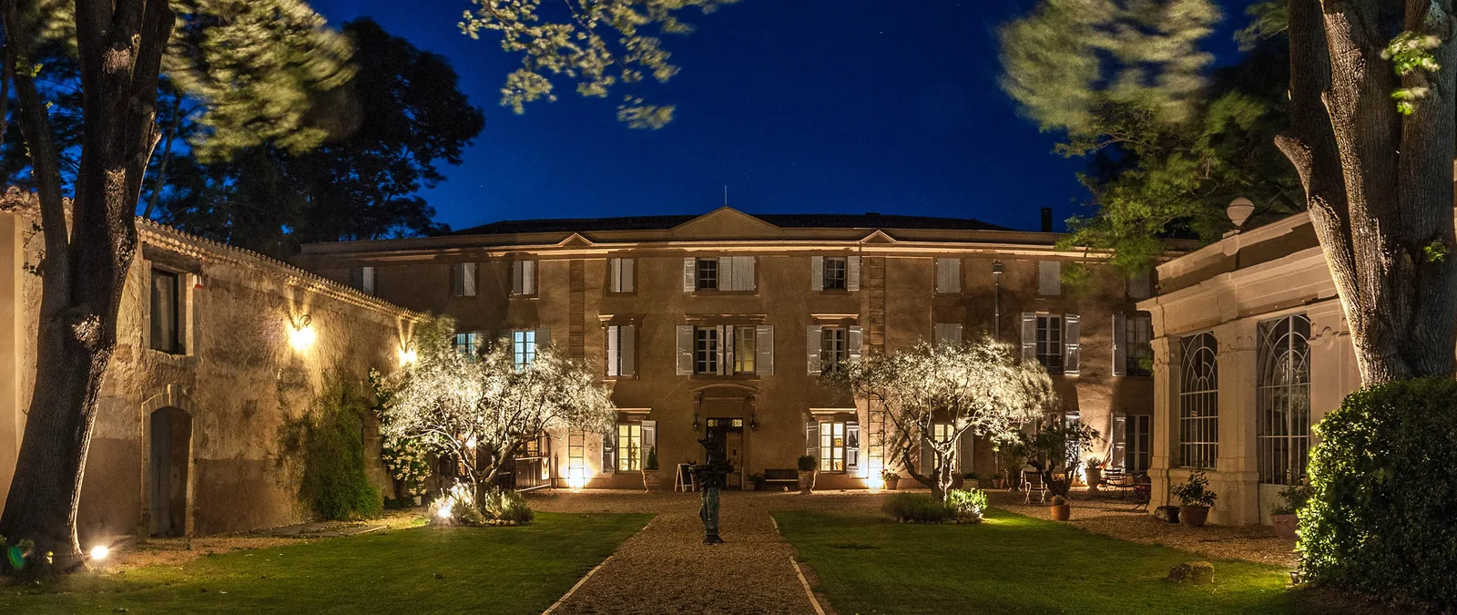 Façade château éclairée, jardin verdoyant, arbres, allée gravier, ambiance nocturne élégante Château Rieutort Saint-Pargoire mariage Hérault Occitanie