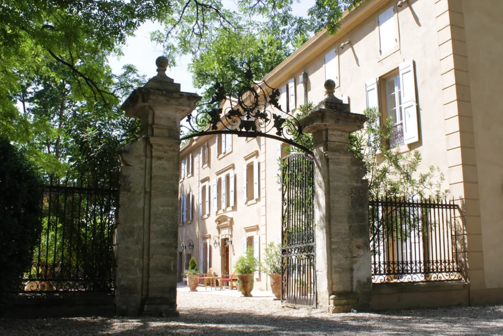 Portail fer forgé, allée graviers, façade château pierre, volets blancs, jardin verdoyant, ambiance élégante Château Rieutort Saint-Pargoire mariage Hérault Occitanie