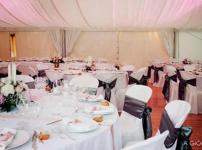 Salle de mariage sous chapiteau décorée avec tables rondes nappes blanches et fleurs roses, Château Hérault