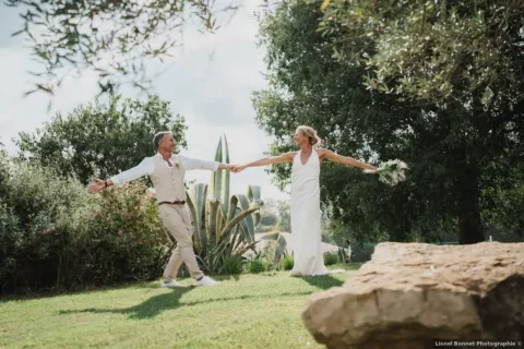 Mariés et famille marchant sur l'allée d'oléandres en fleurs du Domaine de Christin dans l'Hérault lors d'un mariage provençal