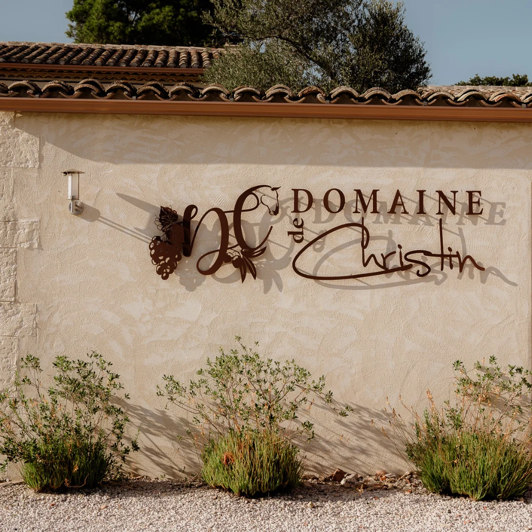 Facade d'entrée du Domaine de Christin avec logo en métal rouille sur mur en pierre en Hérault
