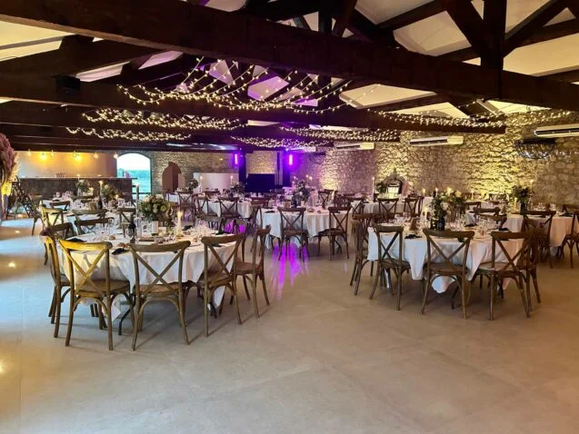 Salle de mariage Domaine de Fangouse Hérault avec guirlandes lumineuses, murs en pierre et tables rondes dressées