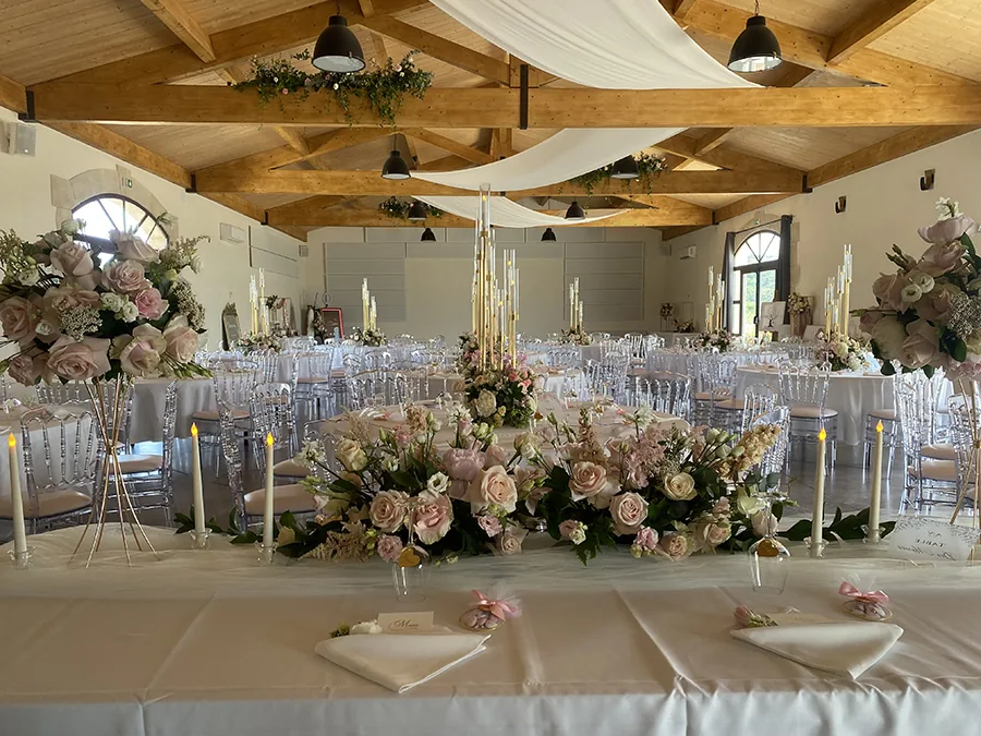 Salle de réception décorée, tables rondes, chaises transparentes, poutres apparentes, ambiance élégante Domaine de la Resclauze Caux mariage Hérault Occitanie