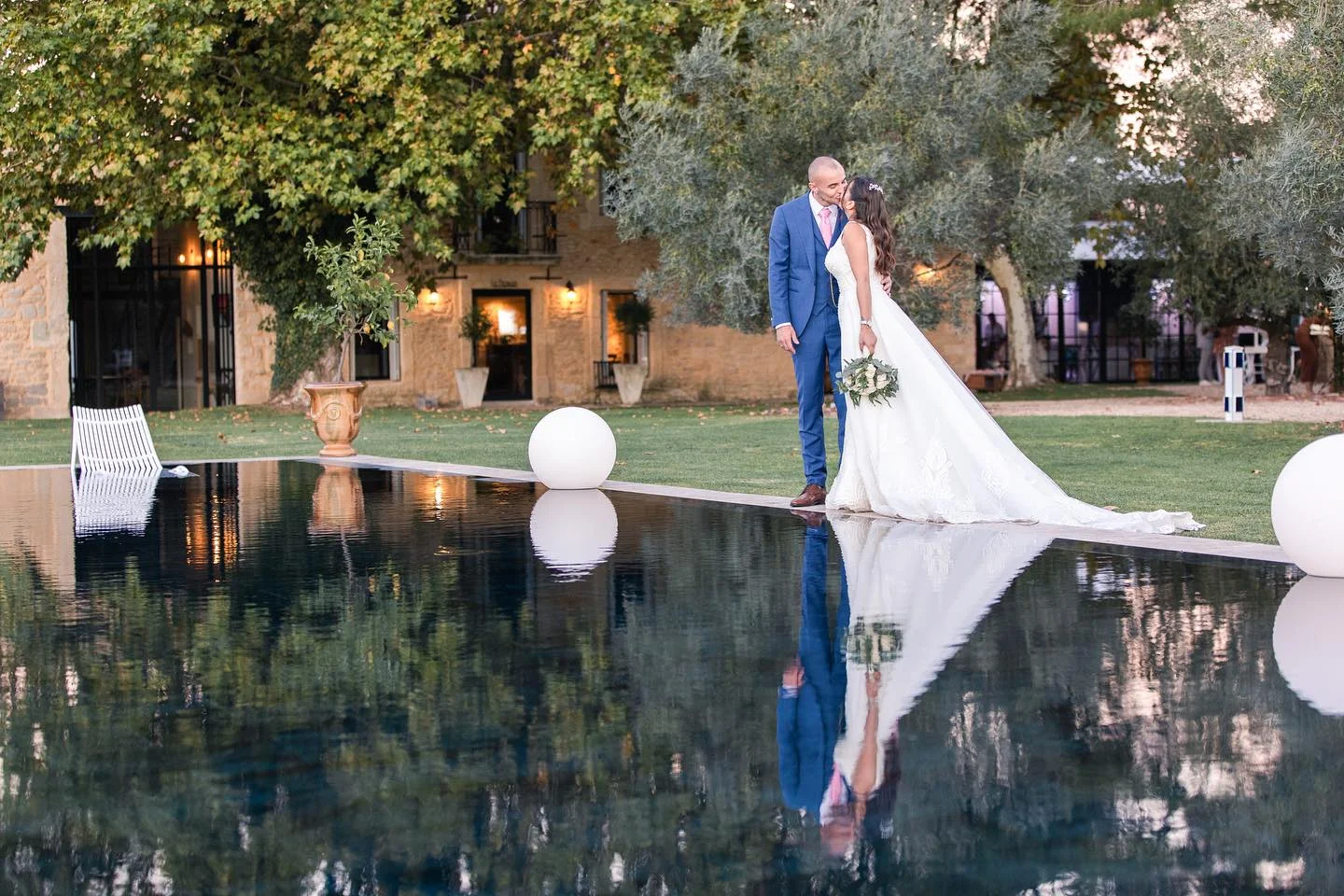Mariés s'embrassant devant la bastide illuminée du Domaine de la Trinité reflétée dans le miroir d'eau, Hérault