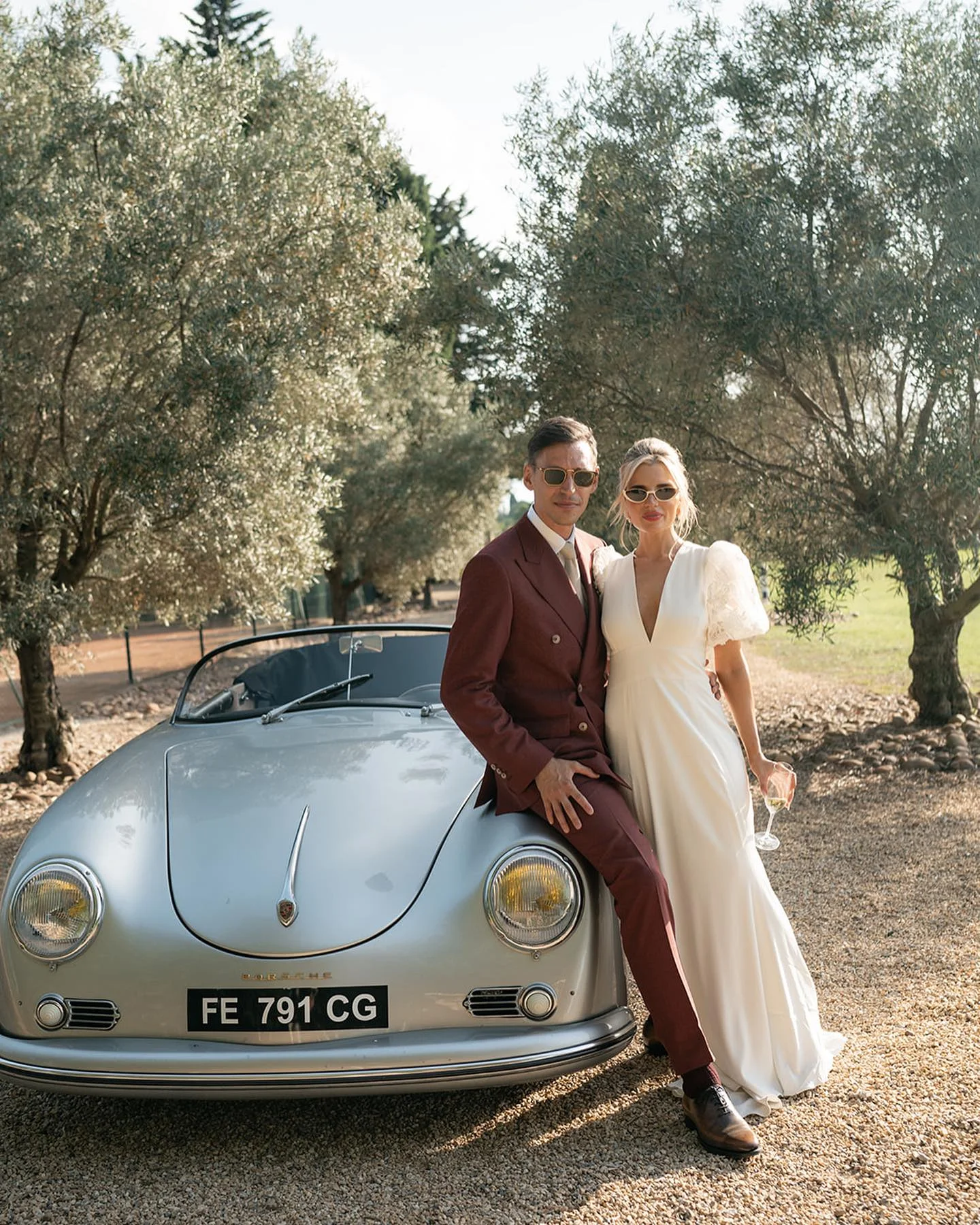 Couple de mariés devant une Porsche 356 cabriolet vintage sous les oliviers du Domaine de la Trinité, Hérault