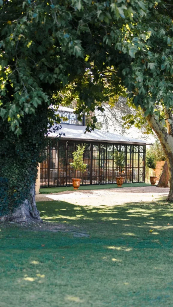 Orangerie en fer forgé du Domaine de la Trinité en Hérault, vue depuis le jardin ombragé avec vasques en terre cuite