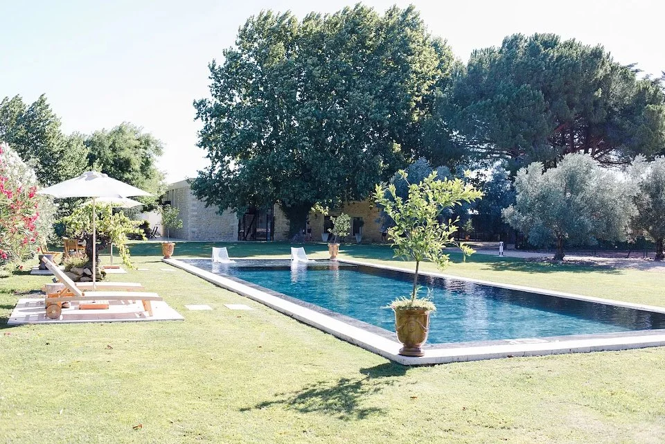 Piscine rectangulaire et jardin verdoyant du Domaine de la Trinité en Hérault, cadre provençal avec transats et bâtisse en pierre