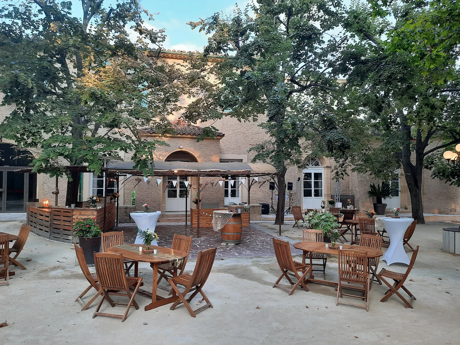 Cour extérieure du Domaine de l'Argentière aménagée pour un cocktail de mariage sous les arbres, Hérault