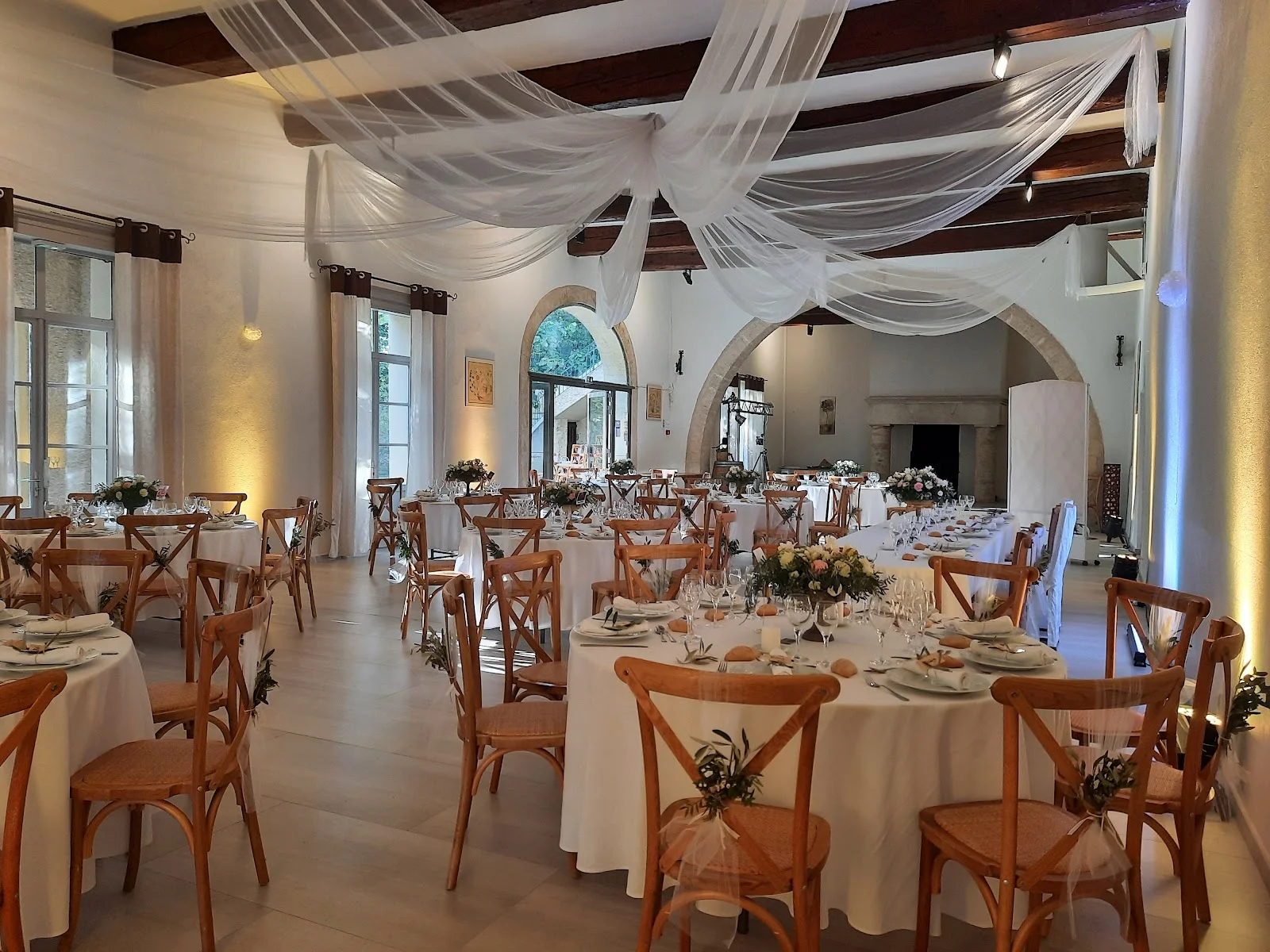 Salle de réception du Domaine de l'Argentière décorée pour un mariage avec voilages blancs et tables fleuries, Hérault