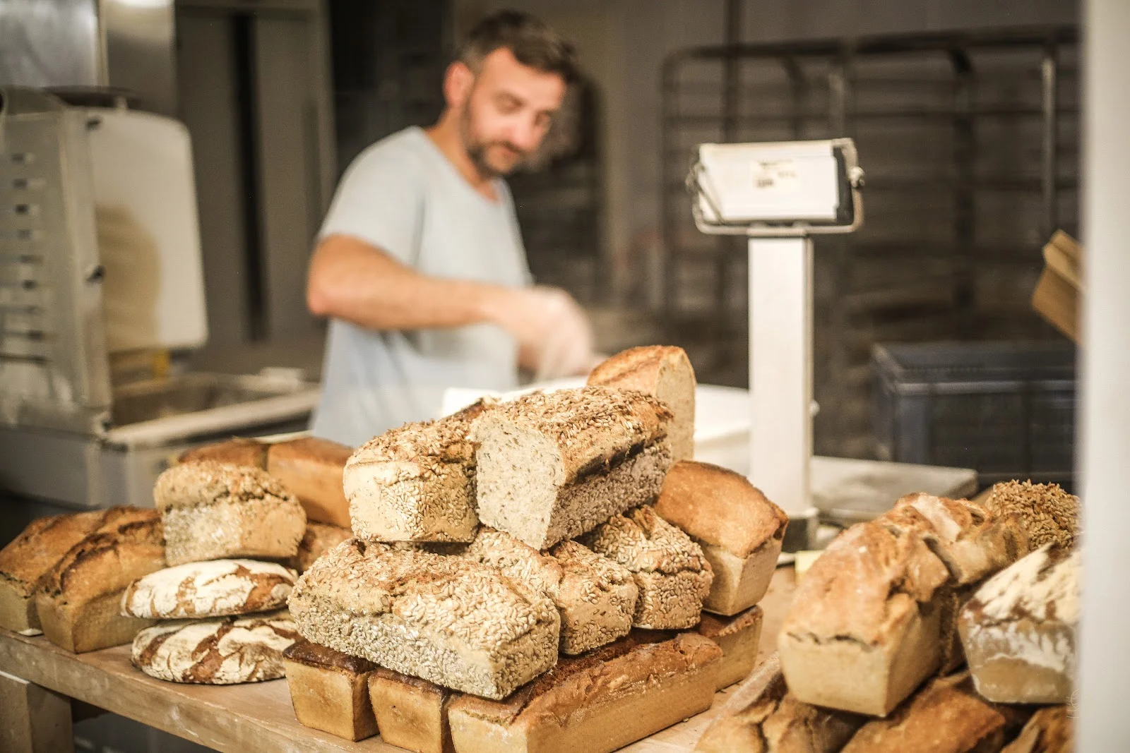 Boulangerie artisanale du Domaine de Montmau avec pains variés au premier plan et boulanger au travail, Hérault