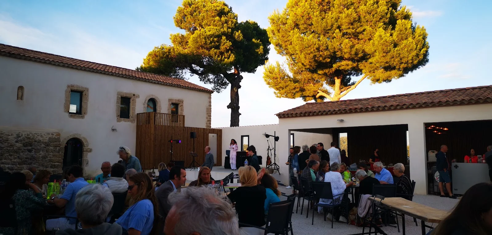 Soirée événementielle en plein air dans la cour du Domaine de Montmau avec convives, scène musicale et pins parasols illuminés, Hérault