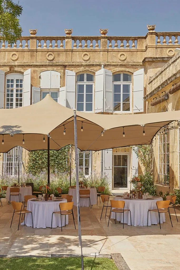 Façade pierre, balustrade, tables rondes dressées sous tente, jardin méditerranéen, ambiance élégante Domaine de Rieucoulon Montpellier mariage Hérault Occitanie