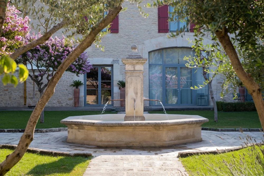 Fontaine provençale en pierre entourée d'oliviers et de lauriers roses dans le jardin du Domaine de Verchant, Hérault