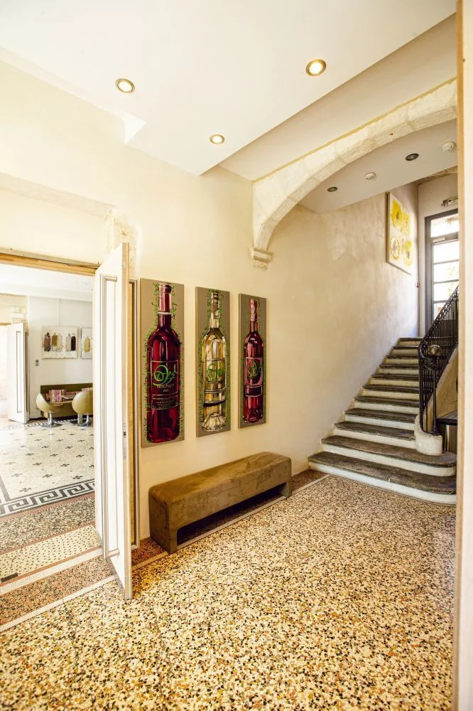 Hall d'entrée du Domaine de Verchant avec triptyque de peintures vins, escalier en pierre et sol terrazzo, Hérault