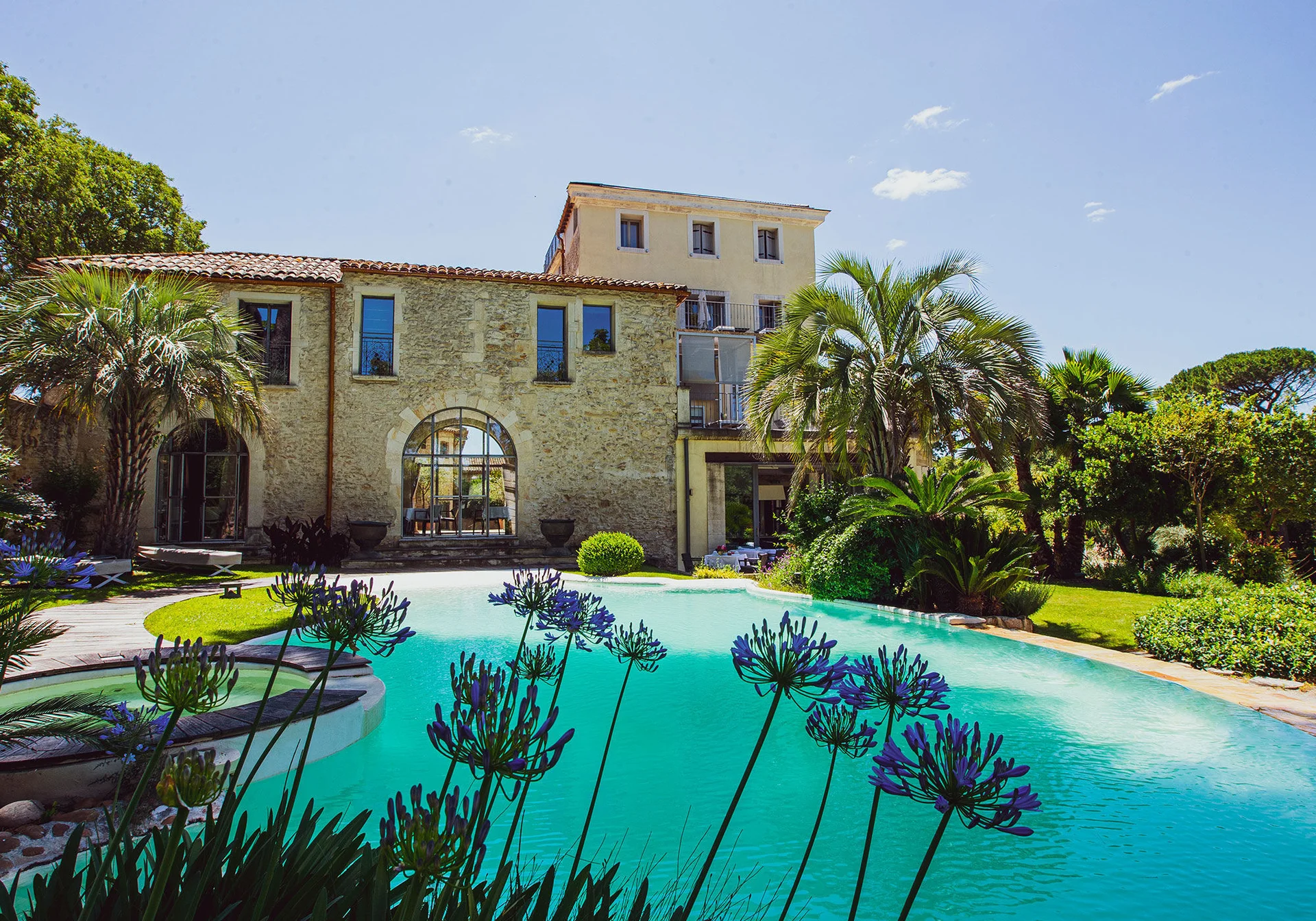 Piscine extérieure du Domaine de Verchant devant le mas en pierre entouré d'agapanthes, Hérault