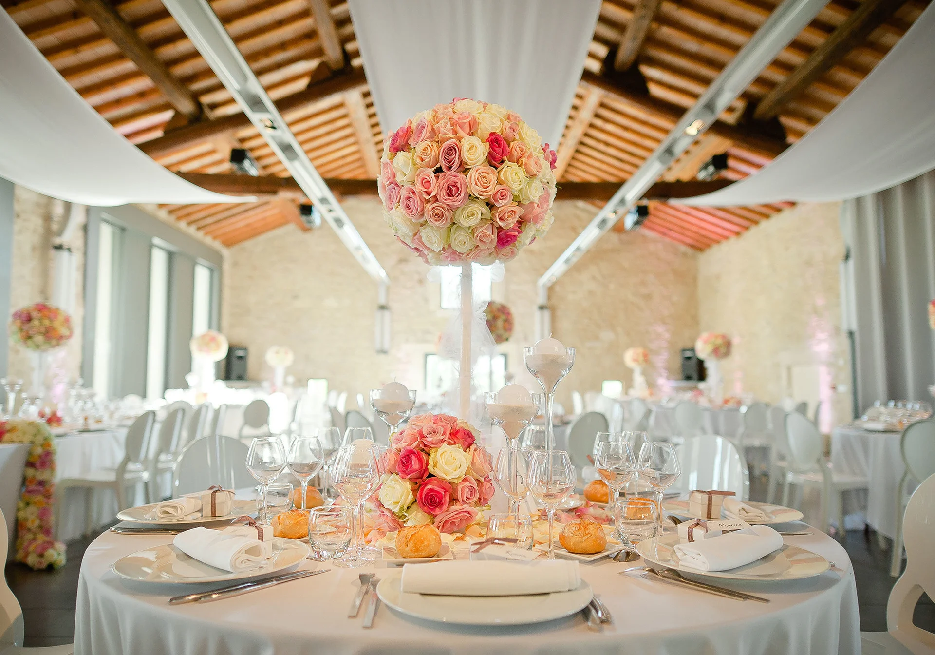 Salle de mariage du Domaine de Verchant décorée avec compositions florales de roses et charpente en bois, Hérault