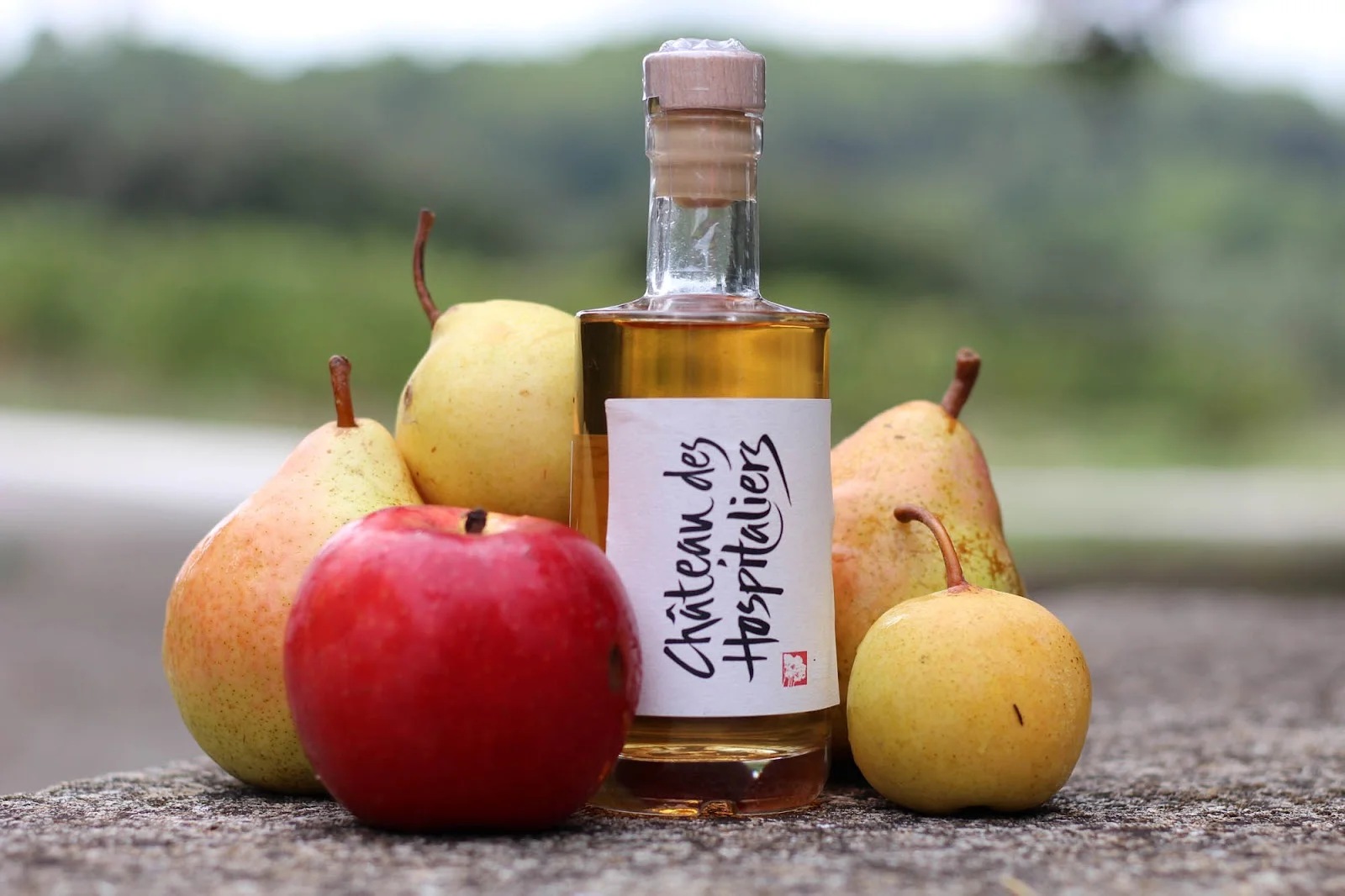Bouteille de liqueur Château des Hospitaliers Hérault entourée de fruits frais pommes et poires du domaine