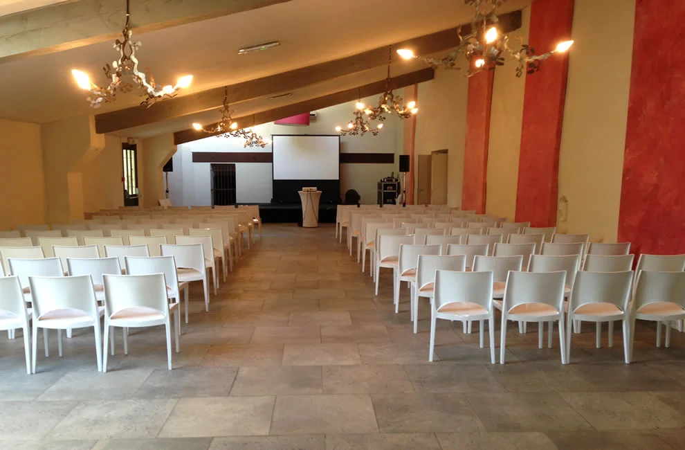Salle de conférence en configuration théâtre au Domaine des Moures avec chaises blanches et écran de projection, Hérault