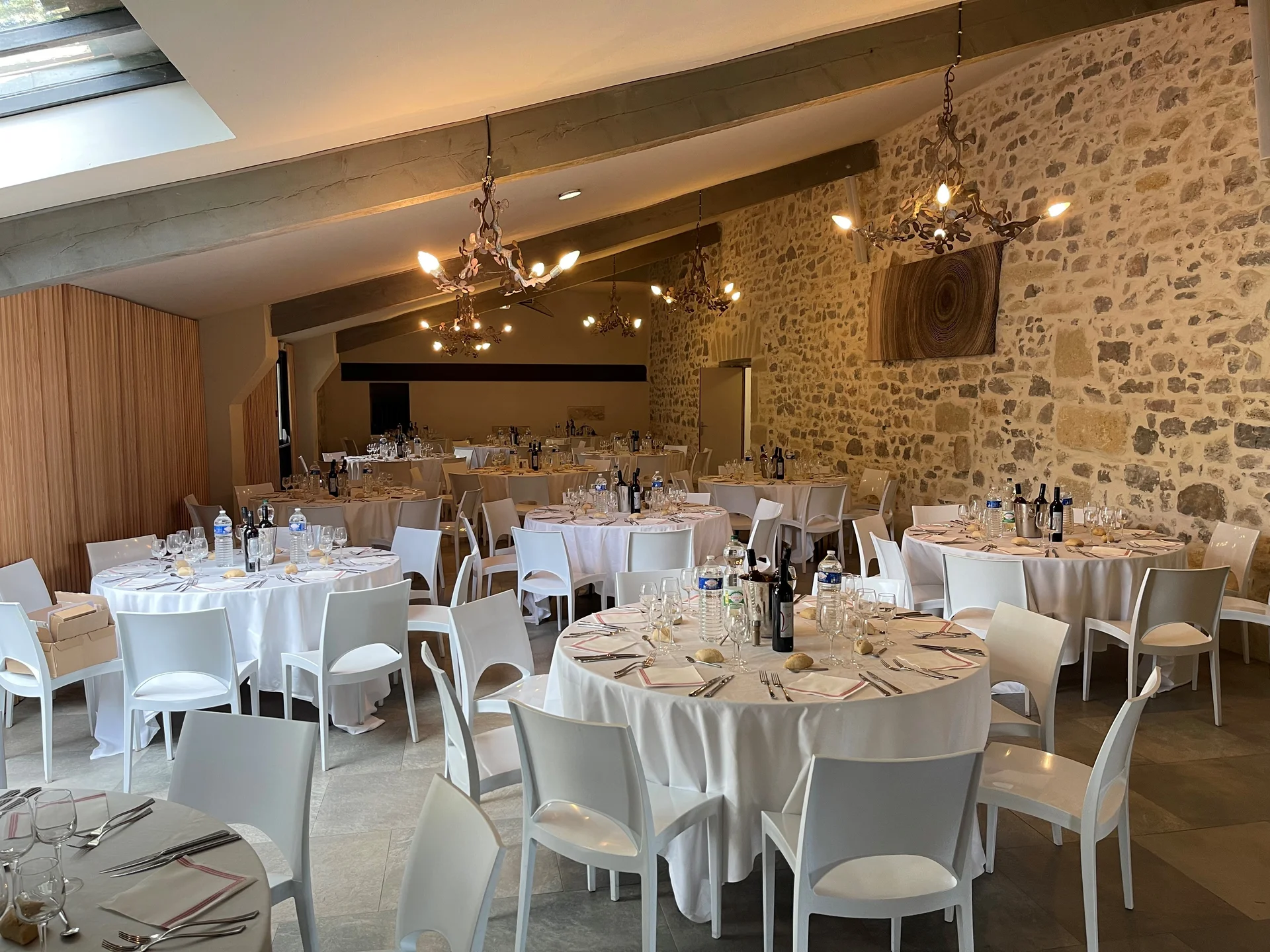 Salle de réception en pierres apparentes du Domaine des Moures avec tables dressées et lustres baroques, Hérault