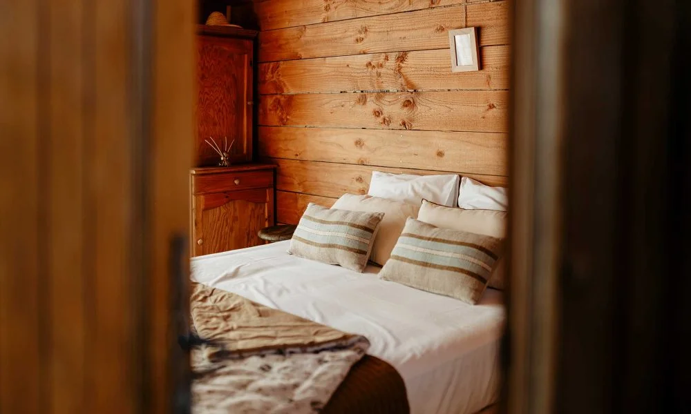 Chambre en bois avec lit double blanc et coussins beige au Domaine des Rives, hébergement mariage Hérault