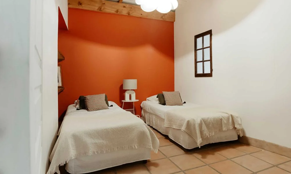 Chambre twin avec mur orange et poutres bois au Domaine des Rives Hérault