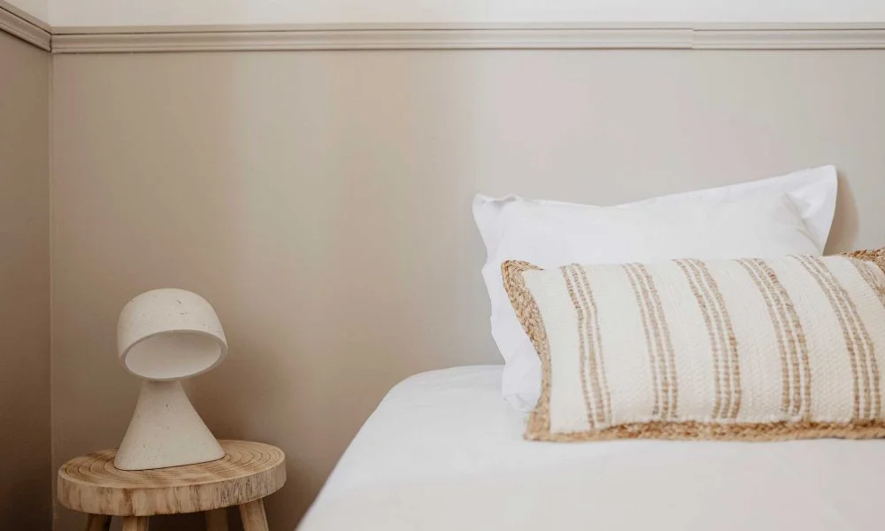 Détail de chambre minimaliste avec coussin naturel et lampe céramique au Domaine des Rives Hérault