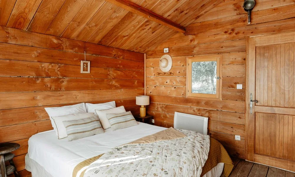 Intérieur chambre cabane dans les arbres avec plafond voûté en bois et lit double blanc au Domaine des Rives Hérault