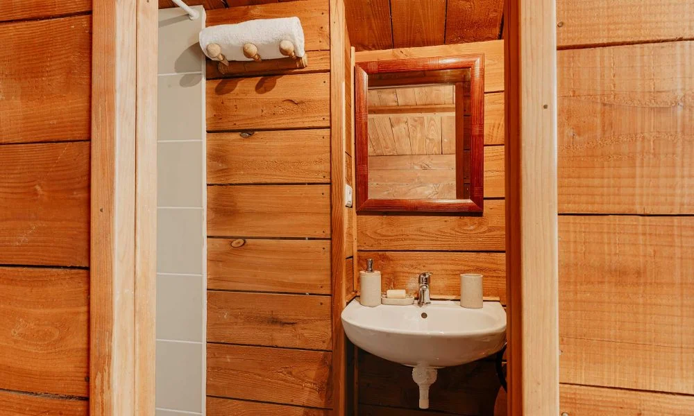Salle de bain en bois avec lavabo blanc et douche dans la cabane du Domaine des Rives, Hérault