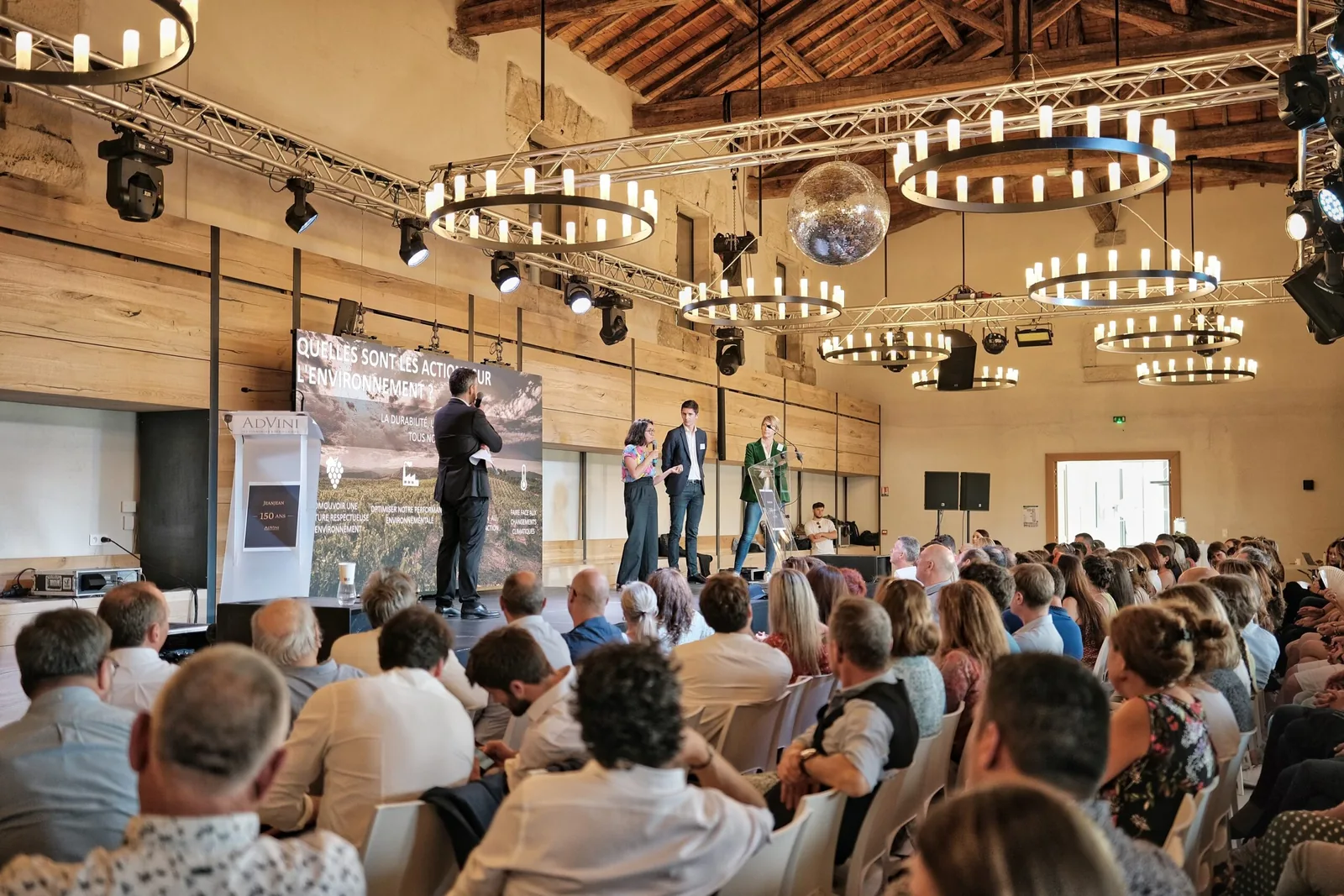 Salle séminaire moderne, poutres apparentes, lustres design, écran géant, conférenciers, public attentif Domaine du Mas Neuf Vic-la-Gardiole séminaire Hérault Occitanie