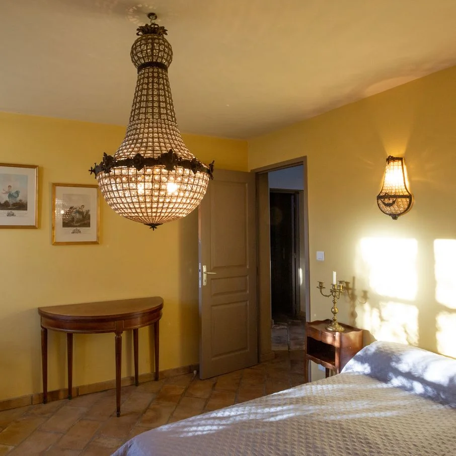 Chambre du Domaine La Fourcade aux murs jaunes, lit double et lustre en cristal