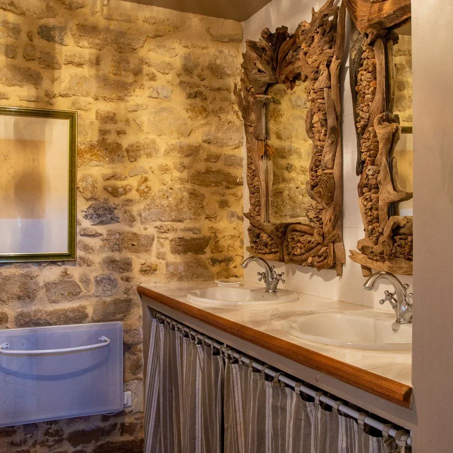 Salle de bain du Domaine La Fourcade, double vasque et miroir doré contre un mur en pierre