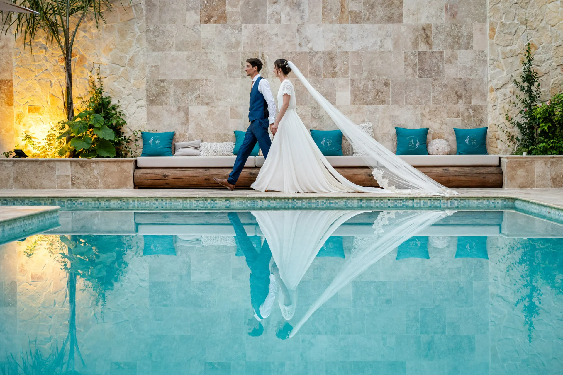 Couple de mariés longeant la piscine avec reflet dans l'eau au Domaine Le Petit Malherbes, Hérault