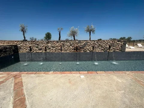 Piscine avec jets d'eau et mur en pierres bordé d'oliviers au Domaine Les Barrettes Agde Hérault